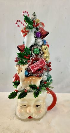 a ceramic christmas tree sitting on top of a cup filled with candy and candies