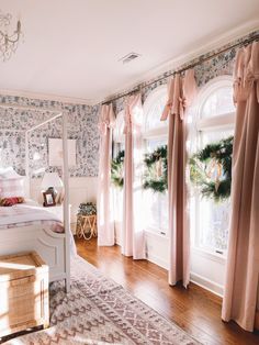 a bedroom decorated for christmas with pink curtains and wreaths on the window sill