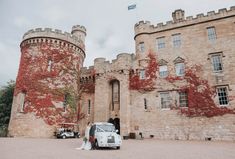 a bride and groom standing in front of an old castle with red leaves on it