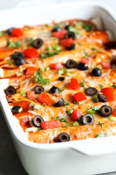 a casserole dish filled with cheese, black olives, tomatoes and green peppers