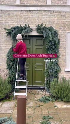 a woman standing on a stepladder in front of a door decorated with christmas wreaths