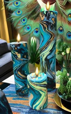 there are peacock feathers on the table and candles in vases next to each other