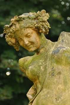 an old statue is sitting in front of some trees