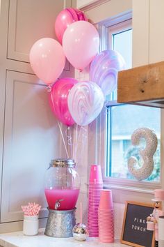 pink and white balloons are in a vase on the counter next to a window sill