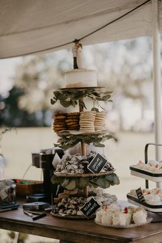 a table topped with lots of cakes and cupcakes next to a white tent