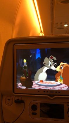 the screen on an airplane shows two cartoon characters, one is kissing and the other is talking