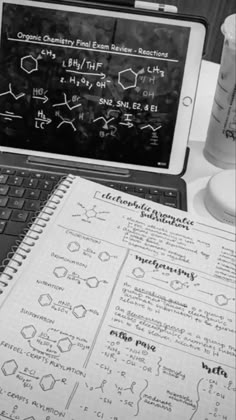 an open laptop computer sitting on top of a desk next to a notebook and cup