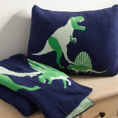 two blue pillows with dinosaurs on them sitting on a dresser next to a pillow case