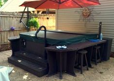 an outdoor hot tub in the middle of a patio with stools under an umbrella