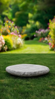 a stone sitting in the middle of a lush green field with flowers and trees behind it