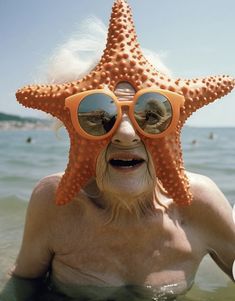 an old man wearing sunglasses and a starfish hat in the water at the beach