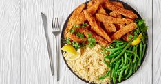 fish fillets with rice, green beans and lemon wedges on a black plate