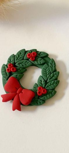 a green wreath with red bows and holly leaves on white surface next to cat toy