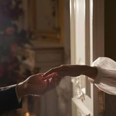 two hands reaching out to each other in front of a door with christmas lights on it