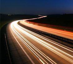 an image of a highway at night with light streaks on the road and trees in the background