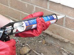 a person in red gloves is holding a piece of construction equipment that has been placed on the side of a brick wall