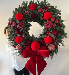 a woman holding a christmas wreath with red balls on it