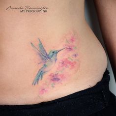 a woman's stomach with a hummingbird tattoo on her side and pink flowers in the back