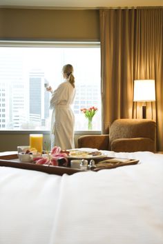 a woman in a bathrobe standing next to a bed with breakfast on it