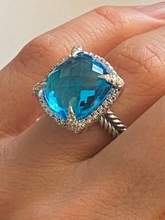 PREVIOUSLY USED  David Yurman CHATELAINE COLLECTION  14mm Blue Topaz & Diamond RingSize 7  Specifications  Estimated Retail $1800  Metal : High Polish 925. Sterling Silver  Gem: Blue Topaz 14mm  X 14mm Checkerboard Faceted Cushion Shape Diamonds: Round Brilliant, Pave Setting, Near Colorless SI clarity Estimated .30ct -.35ct Total  Signature: Inside The Band (c) DY Hallmark: 925 Condition: Very Good Collateral : Pouch  Guarantee : YES 100% Luxury Diamond Topaz Ring With Cushion Cut, Luxury Cushion Cut Diamond Topaz Ring, Luxury Topaz Ring With Accent Stones, Luxury Topaz Ring With Diamond Accents, Luxury Cushion Cut Topaz Ring For Anniversary, Luxury Blue Topaz Ring With Diamond Accents, Luxury Blue Topaz Cushion Cut Ring, Luxury White Gold Topaz Ring With Halo Setting, Luxury Topaz Ring With Halo Setting