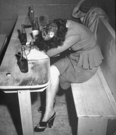 a woman sitting at a table with her head in a glass bottle and looking down