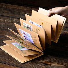 a person is holding several folders open on a wooden table with their hand reaching for them