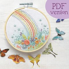 an embroidery project with butterflies and flowers on the table, next to it is a colorful rainbow