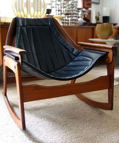 a black leather rocking chair sitting on top of a carpeted floor next to a table