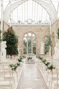 an indoor wedding venue with white chairs and greenery on the aisle, surrounded by statues