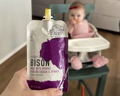 a baby sitting in a highchair and holding up a bag of bison milk