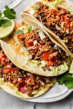 three tacos on a plate with lime wedges