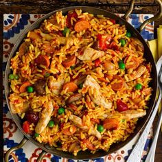 a pan filled with chicken and rice on top of a table next to silverware