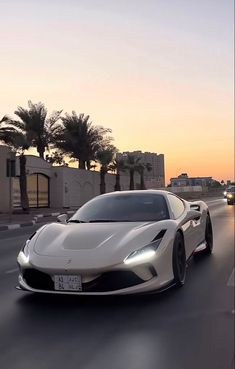 a white sports car driving down the road at dusk with palm trees in the background