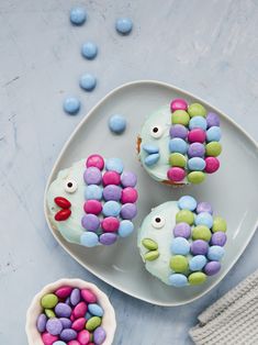 three cupcakes decorated like fish on a plate with candy candies around them