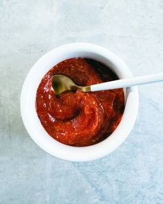 a white bowl filled with red sauce and a spoon on top of blue countertop