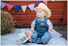 a little boy sitting on the ground with cake in his mouth and straw bales behind him