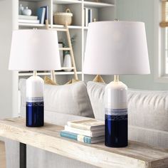 two lamps sitting on top of a wooden table in front of a white book shelf