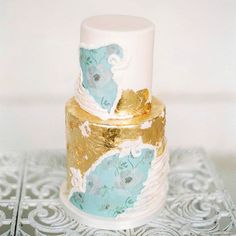 a three tiered cake with gold and blue designs on the top is sitting on a silver tray