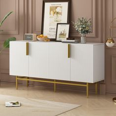 a white and gold sideboard in a living room next to a potted plant