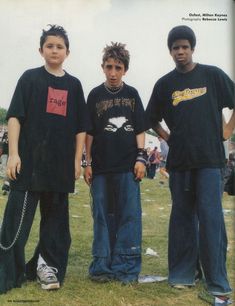 three young men standing next to each other on top of a grass covered field with people in the background