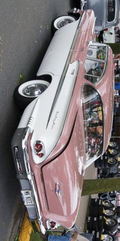 an old pink and white car parked next to other cars