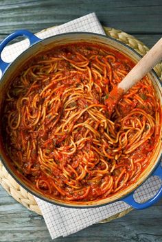 a blue pot filled with spaghetti and sauce on top of a wooden table next to a napkin