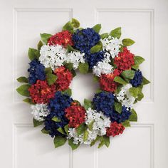 a wreath with red, white and blue flowers is hanging on the front door wall