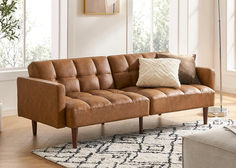 a brown leather couch sitting on top of a wooden floor next to a white rug