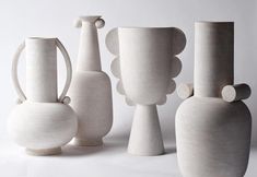 several white vases are lined up against a white background, one is empty and the other has two smaller ones