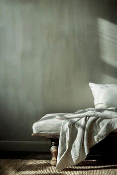 an unmade bed with white linens and pillows on it in front of a gray wall