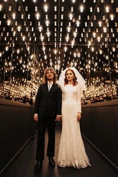 a bride and groom are standing in front of a large chandelier filled with lights