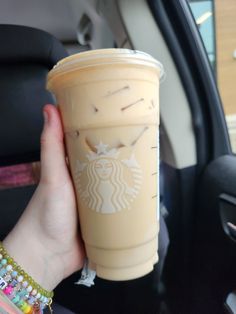 a woman holding up a starbucks cup in her car