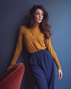 a woman leaning against a wall with her hands on her hips, wearing blue and yellow pants