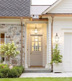 a white house with a gray door and two plants on the front porch next to it